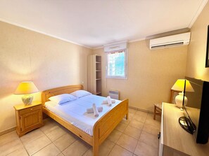 A bedroom with a wooden bed, two bedside lamps, a wardrobe, an air conditioning unit, and a window with a view. - La Terrasse du Lac (Fréjus)