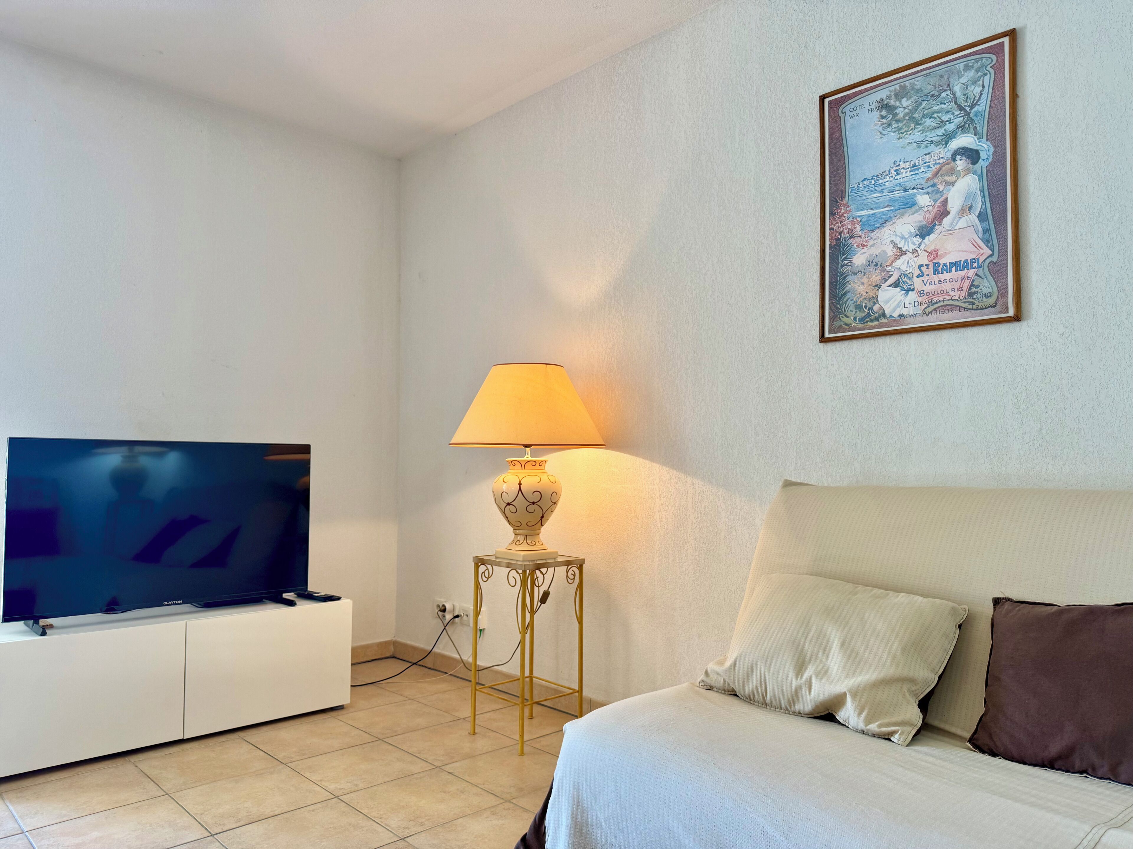 A bedroom with a television on a cabinet, a lamp on a side table, and a bed with pillows.
