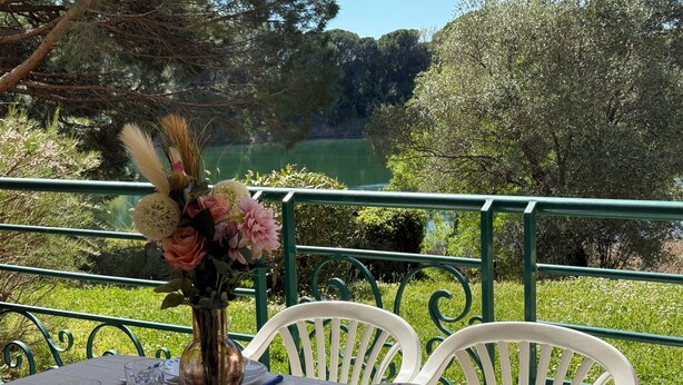 Une table dressée à l’extérieur, avec vue sur un lac, entourée de verdure et de chaises blanches.