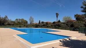 Une piscine d’un bleu éclatant, bordée d’une terrasse carrelée, entourée de verdure et surplombée par un ciel dégagé.