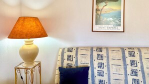 Une pièce avec une lampe sur une petite table, un tableau encadré au mur et un canapé à motifs.