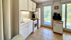 Une cuisine avec des meubles blancs, une cuisinière, un réfrigérateur et une machine à café.