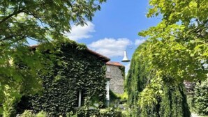 A stone building partially covered with ivy, surrounded by well-maintained greenery and a clear blue sky. - Les Hirondelles du Marais (Riom)