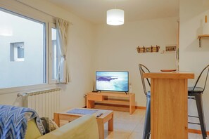 Ein Wohnzimmer mit Fernseher, Holzmöbeln, einem Fenster mit Vorhängen und einer Heizung.