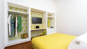 Een slaapkamer met een bed, een televisie en inbouwplanken met kleding en een laptop.