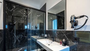 Een moderne badkamer met een witte wastafel, zwarte marmeren wanden en een haardroger bevestigd aan de muur.