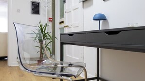 A clear chair, a desk with drawers, a blue lamp, and a potted plant. - The Hove Retreat | Sleeps 10 | 4BR Coastal Escape (Brighton and Hove)