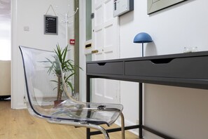 Ein heller Stuhl, ein Schreibtisch mit Schubladen, eine blaue Lampe und ein Blumentopf.