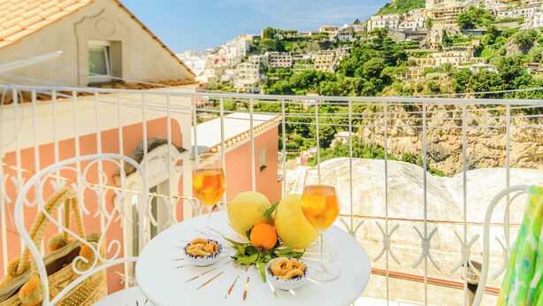 A balcony with a table set for two, overlooking a hillside town. - YourHome - Casa Giulia (Positano)
