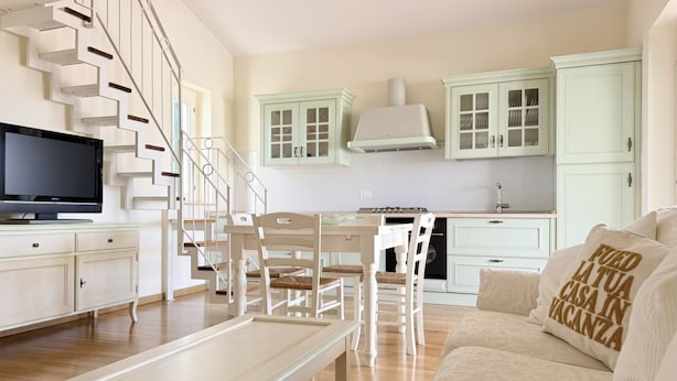 Een moderne woonkamer met een flatscreen televisie, een eethoek met tafel en stoelen, een trap en lichtgroene kastjes.