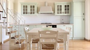 Een keuken met witte kasten, een fornuis en een eettafel met stoelen.
