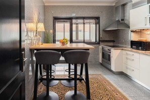 A modern kitchen with a dining area, featuring a kitchen island with stools, a microwave, oven, and a large window with blinds. - Oceanfront & Modern Elegance by HostWise (Vila do Conde)