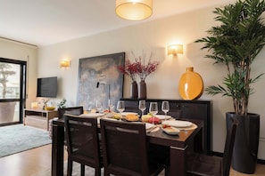 A dining area with a table set for four, a large vase with red flowers, a tall plant, and a painting on the wall. - Oceanfront & Modern Elegance by HostWise (Vila do Conde)