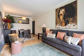 A modern living room with a grey sofa, a dining table, and a large abstract painting. - Oceanfront & Modern Elegance by HostWise (Vila do Conde)