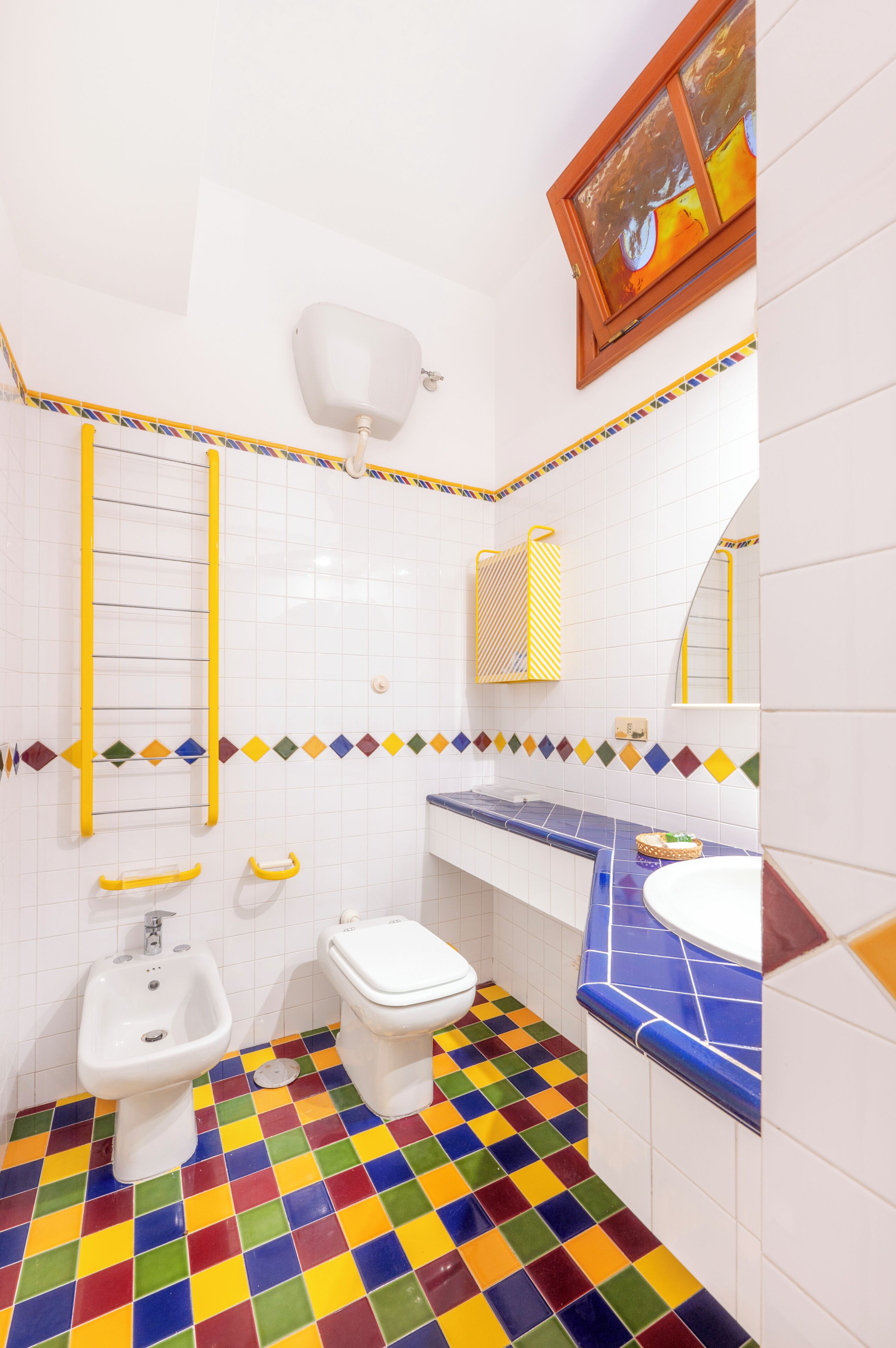 Un baño con piso de cuadros coloridos, un lavamanos blanco, un inodoro y un bidé.