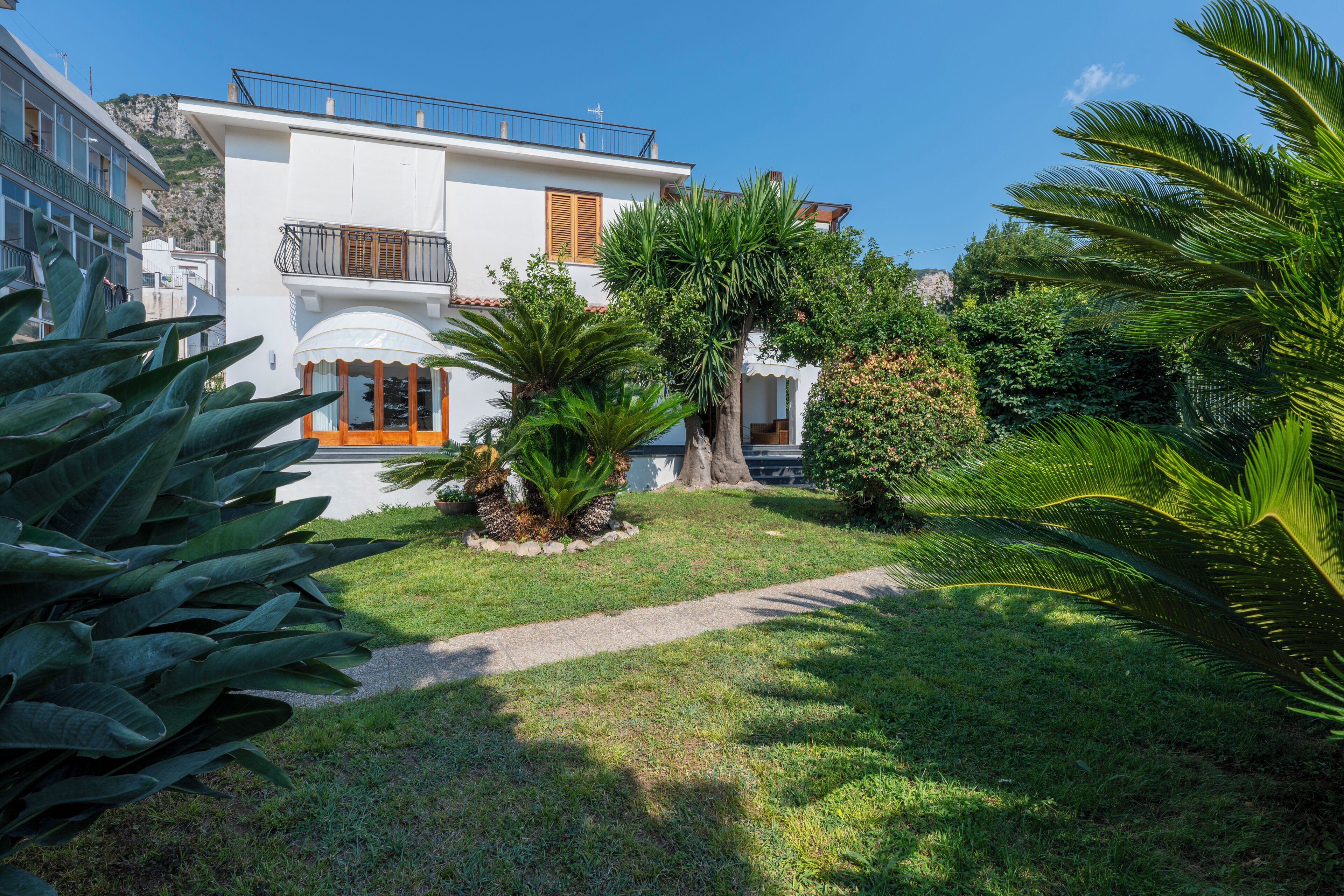 Un bâtiment blanc doté de balcons, un jardin planté de palmiers et un ciel d’un bleu limpide.