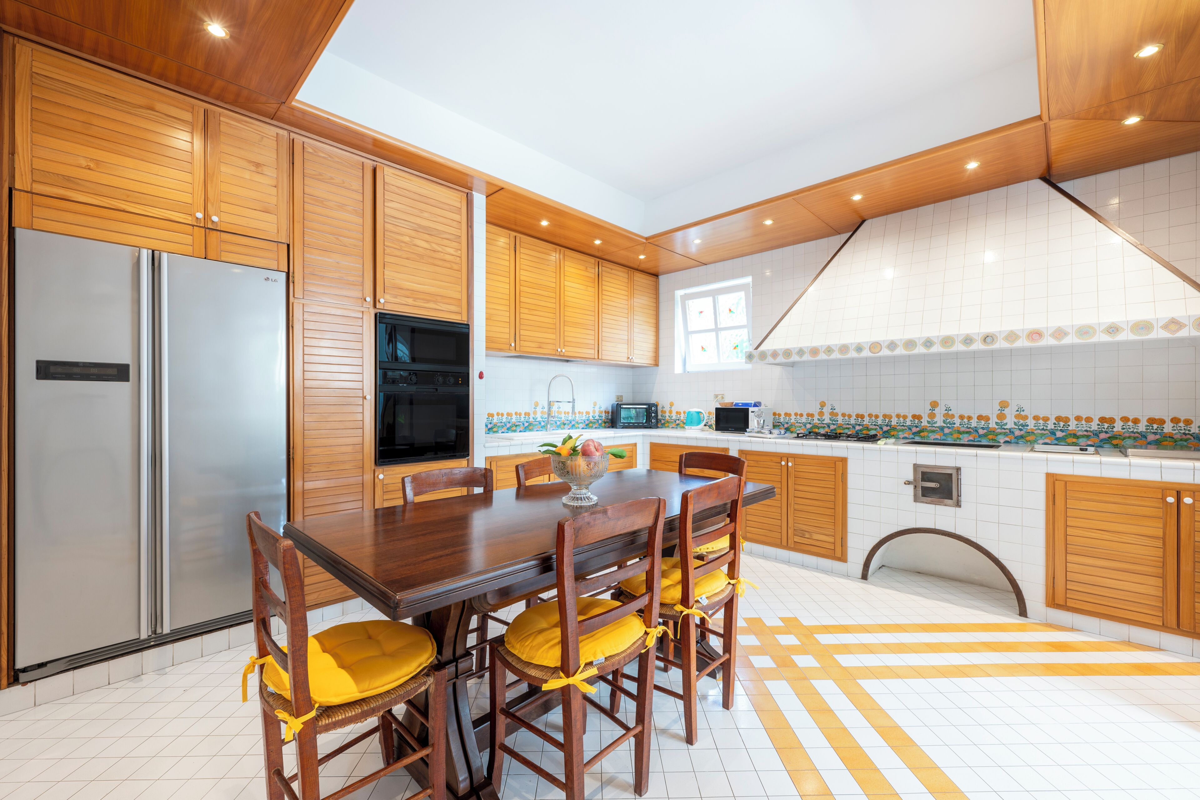 A modern kitchen with wooden cabinets, stainless steel appliances, and a dining area with yellow chairs.