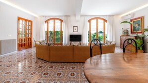 Ein Wohnzimmer mit einer Couch, einem Fernseher, einem Esstisch und Blick auf Grünfläche.