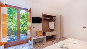 Ein Hotelzimmer mit Schiebetür zu einem Garten, einem Bett mit gerolltem Handtuch, einer Holzbank, einem an der Wand befestigten Fernseher und einem Holzschrank.
