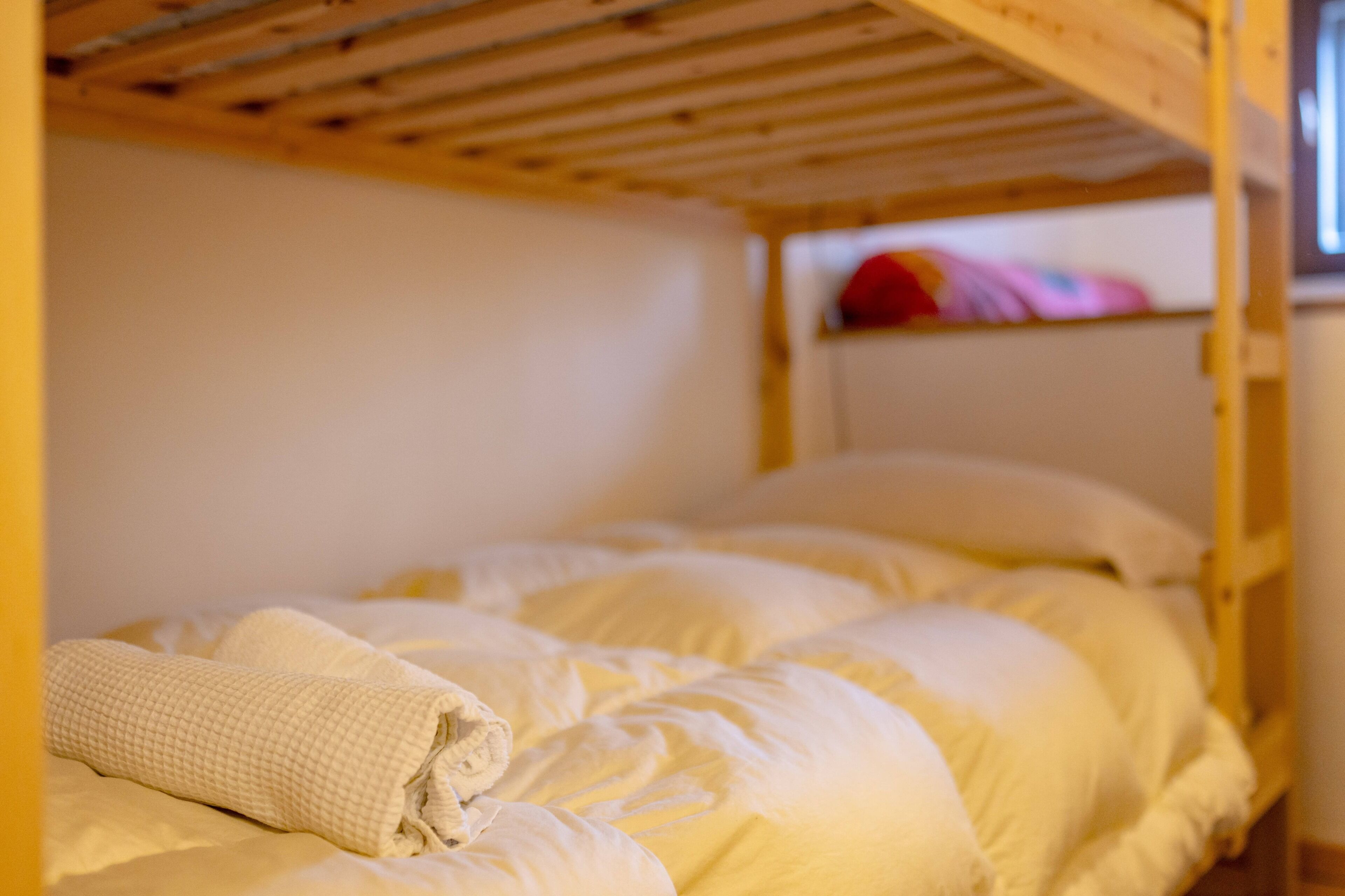 A bunk bed with white bedding, a wooden ceiling, and a window with a view.