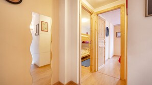 Een hal met houten vloer, een spiegel, een klok en een deur naar een slaapkamer met een bed en een garderobe.