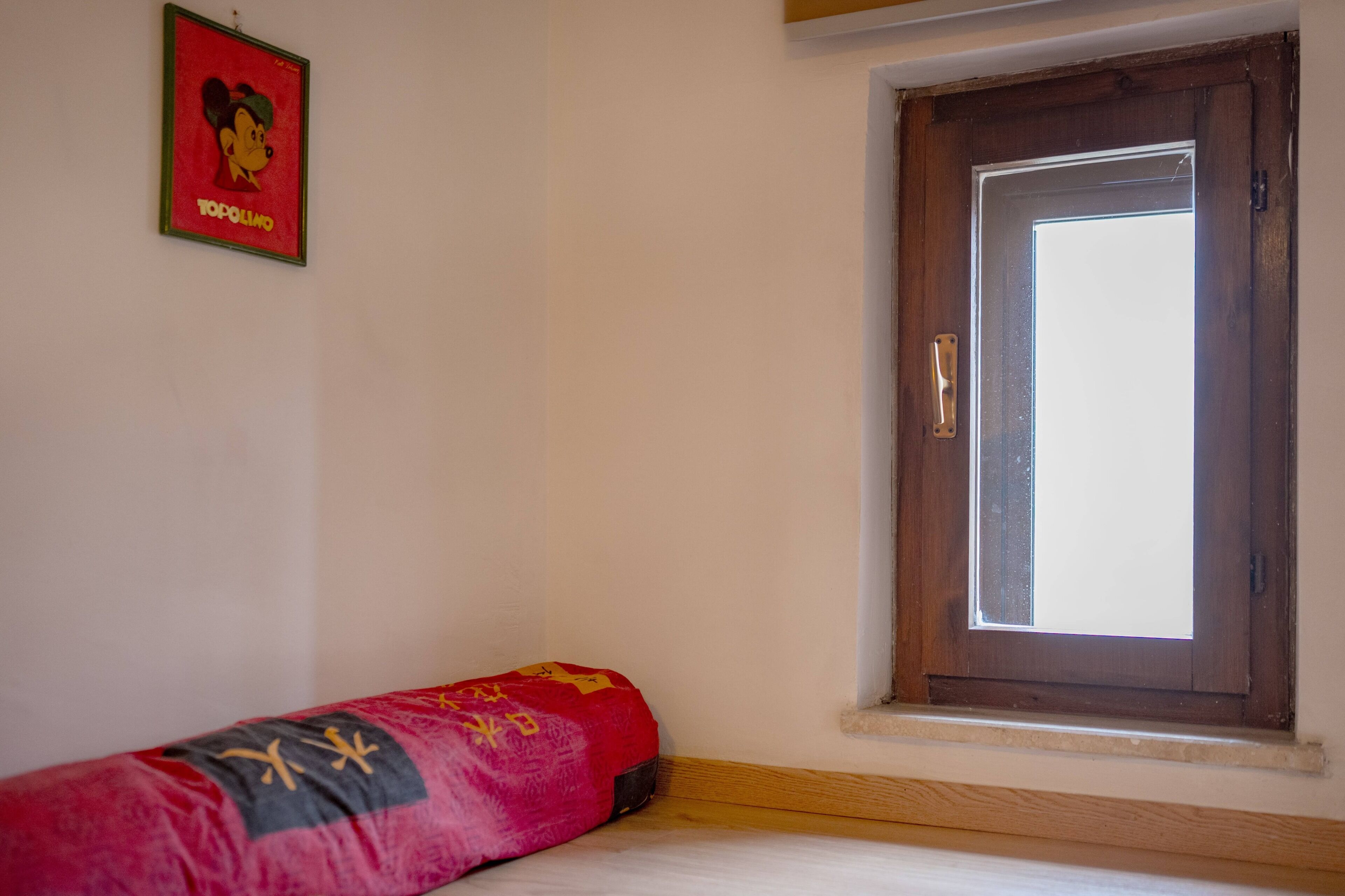 Una stanza con un letto, una finestra con stipite in legno e un quadro appeso al muro.