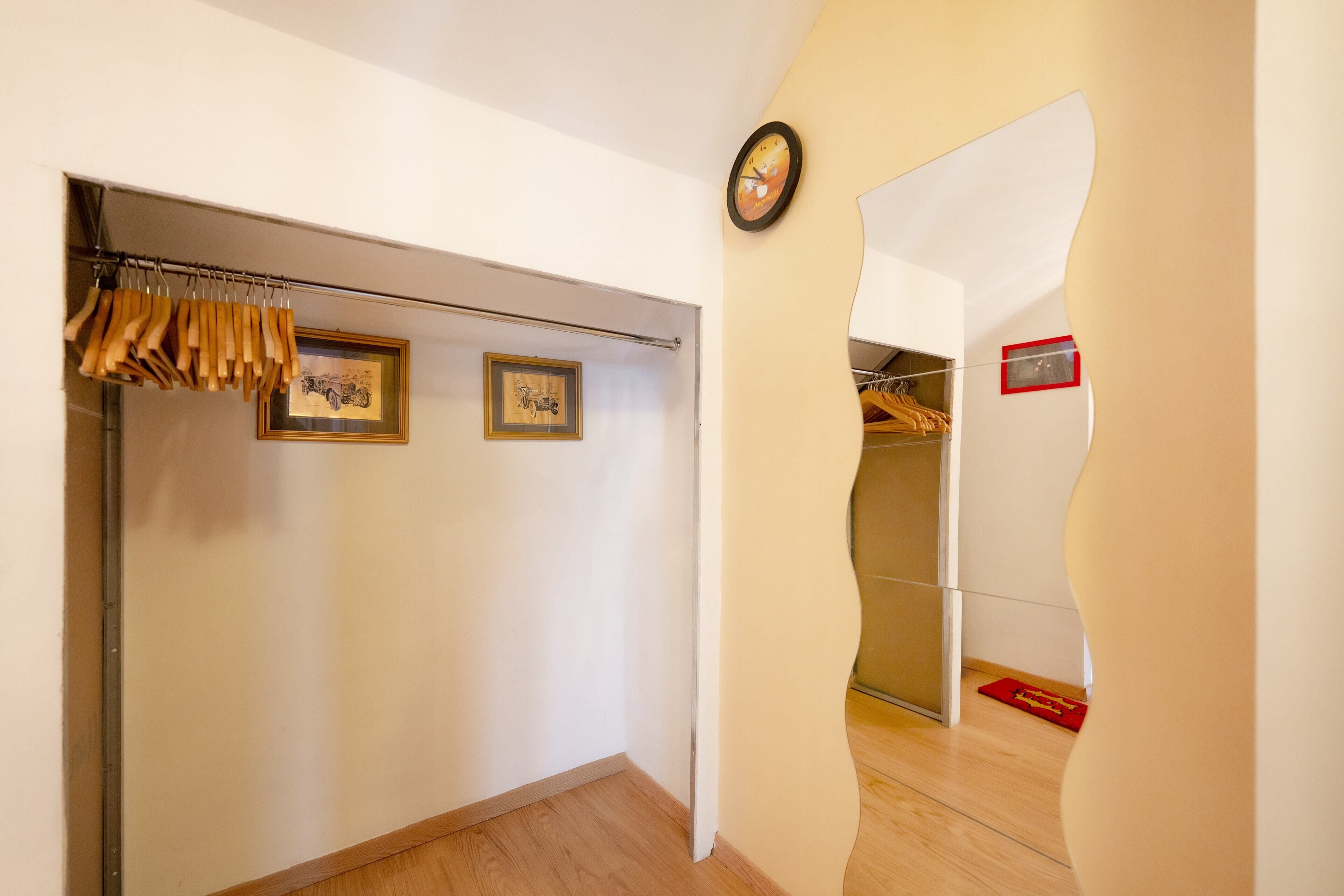 A hallway with a coat rack, framed pictures, a clock, and a red mat on the floor.