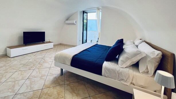 Une chambre à coucher avec un lit, un téléviseur posé sur un meuble, une fenêtre et un luminaire au plafond.