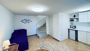 Un espace de vie compact comprenant un canapé, une table à manger, un coin cuisine avec un four à micro-ondes et un escalier menant à un autre niveau.