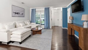 Ein Wohnzimmer mit Ecksofa, Couchtisch, Fernseher und einer blauen Akzentwand.