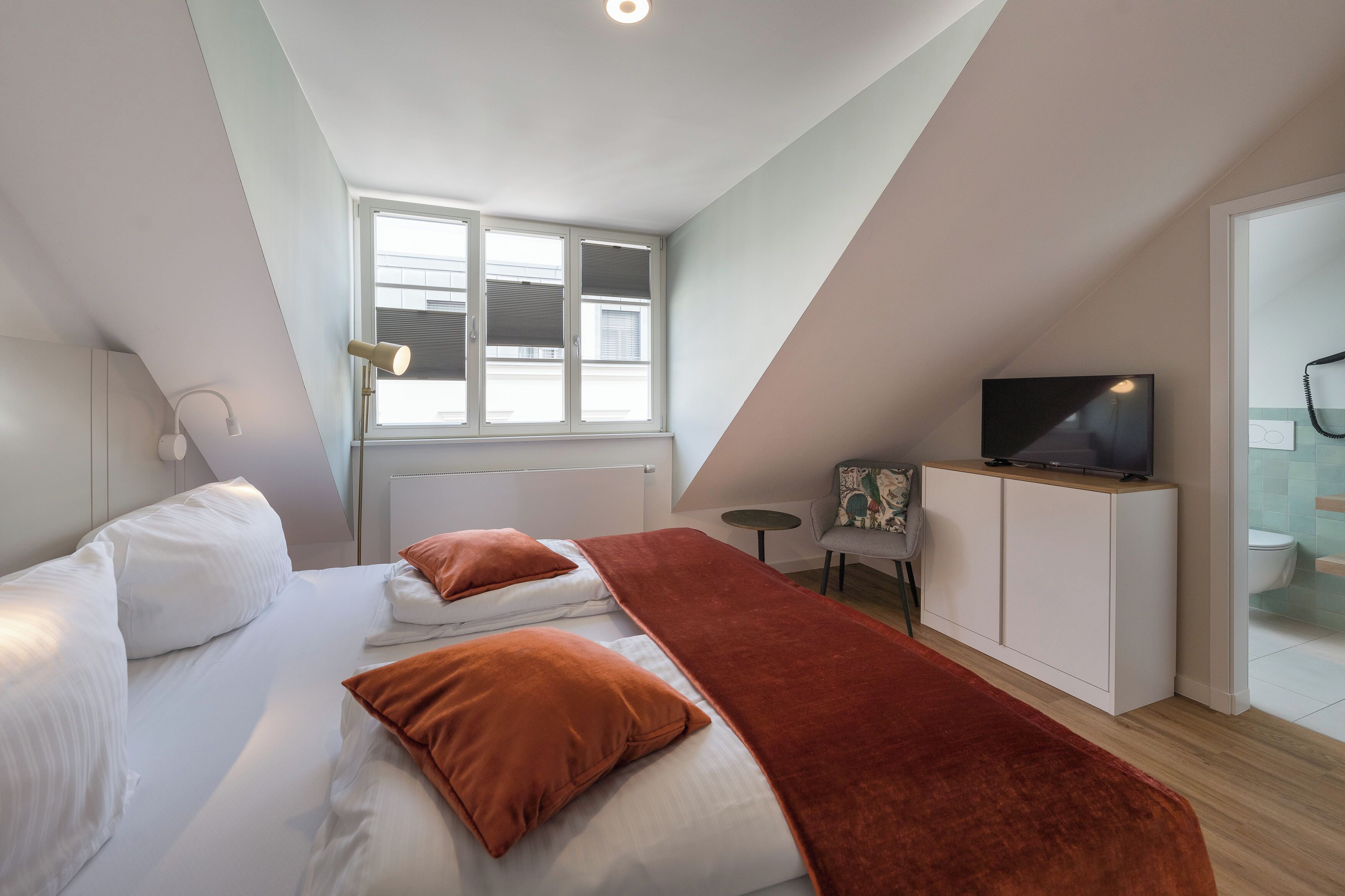 A modern bedroom with a bed, a TV, a small table, and a window.