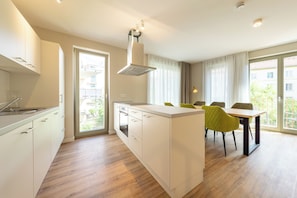 A modern kitchen with a central island, built-in oven, and large windows. - Design Apartments - Luise (Potsdam)