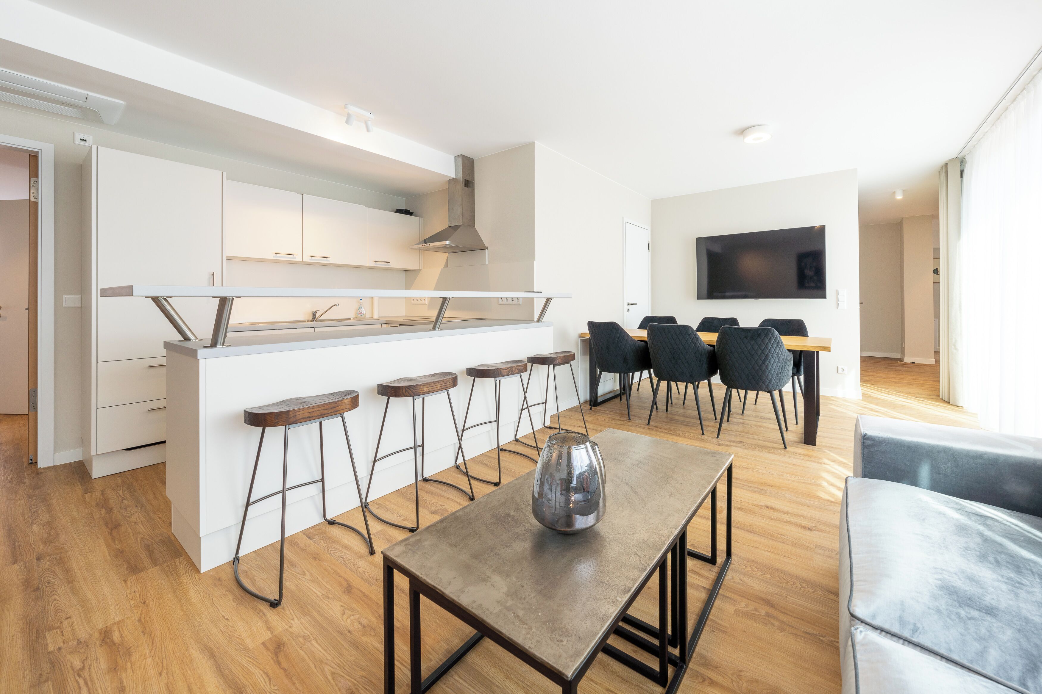 A modern kitchen with white cabinets, a central island with stools, and a dining area with a table and chairs.