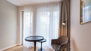 Una habitación con una mesa redonda, una silla, una lámpara y un ventanal con cortinas.