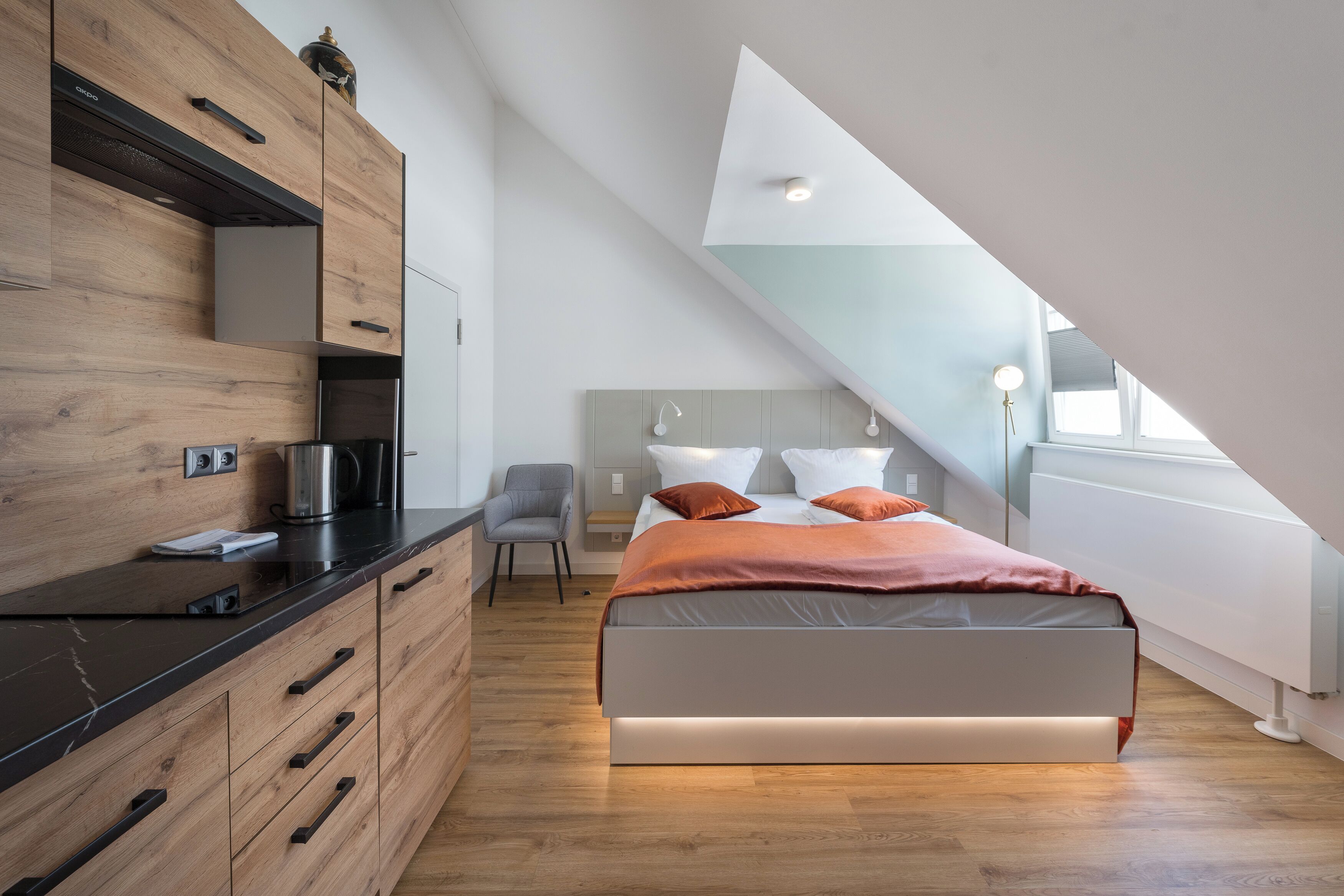 Un dormitorio moderno con techo estilo loft, una cama con ropa de cama naranja, un escritorio con hervidor y una silla.