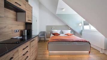 Un dormitorio moderno con techo estilo loft, una cama con ropa de cama naranja, un escritorio con hervidor y una silla.