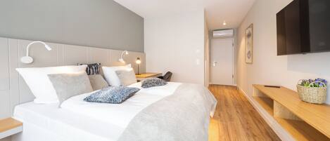Um quarto moderno com uma cama grande, mesas de cabeceira, uma televisão e chão de madeira.