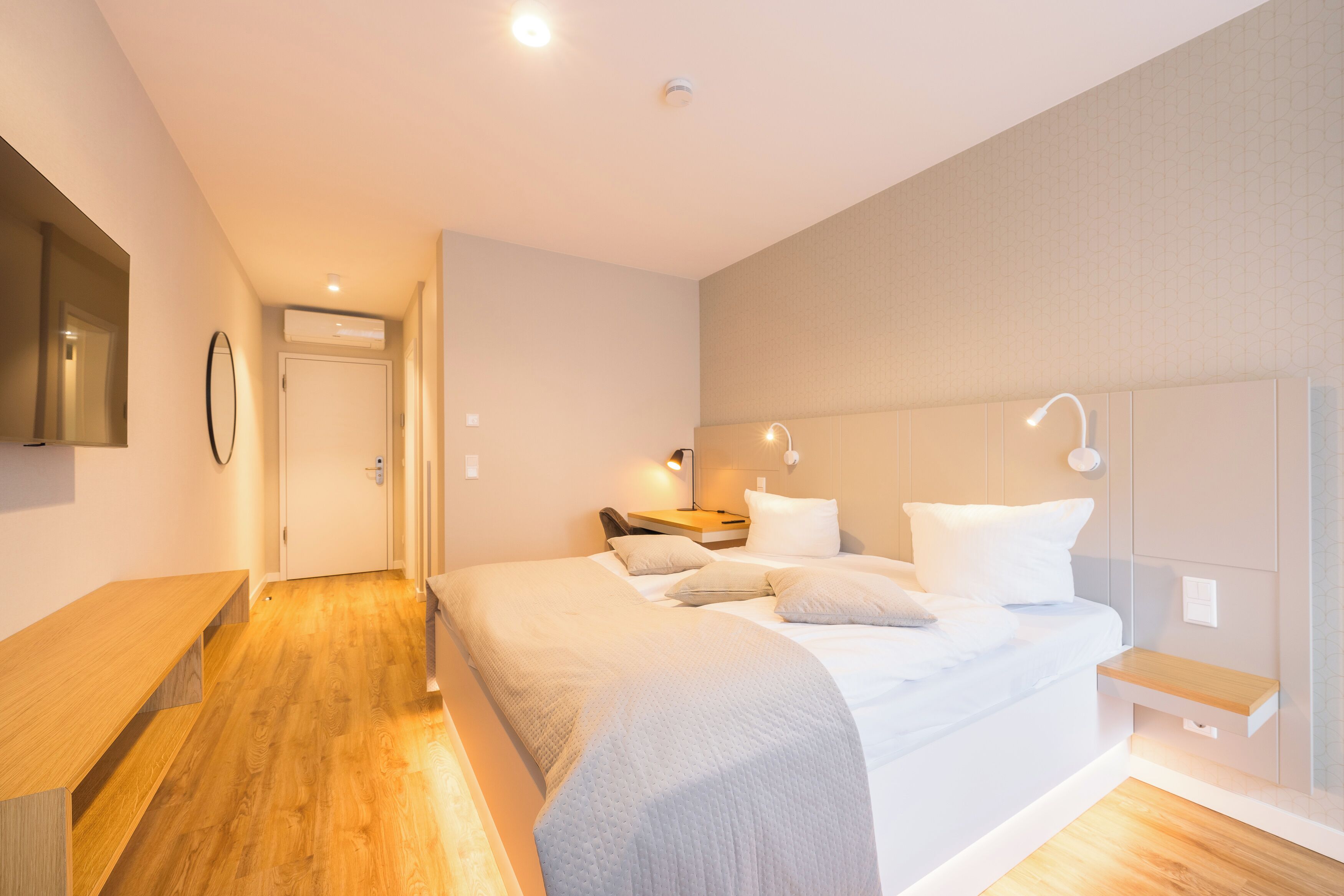 A modern hotel room with a large bed, bedside tables, a desk, and a TV.