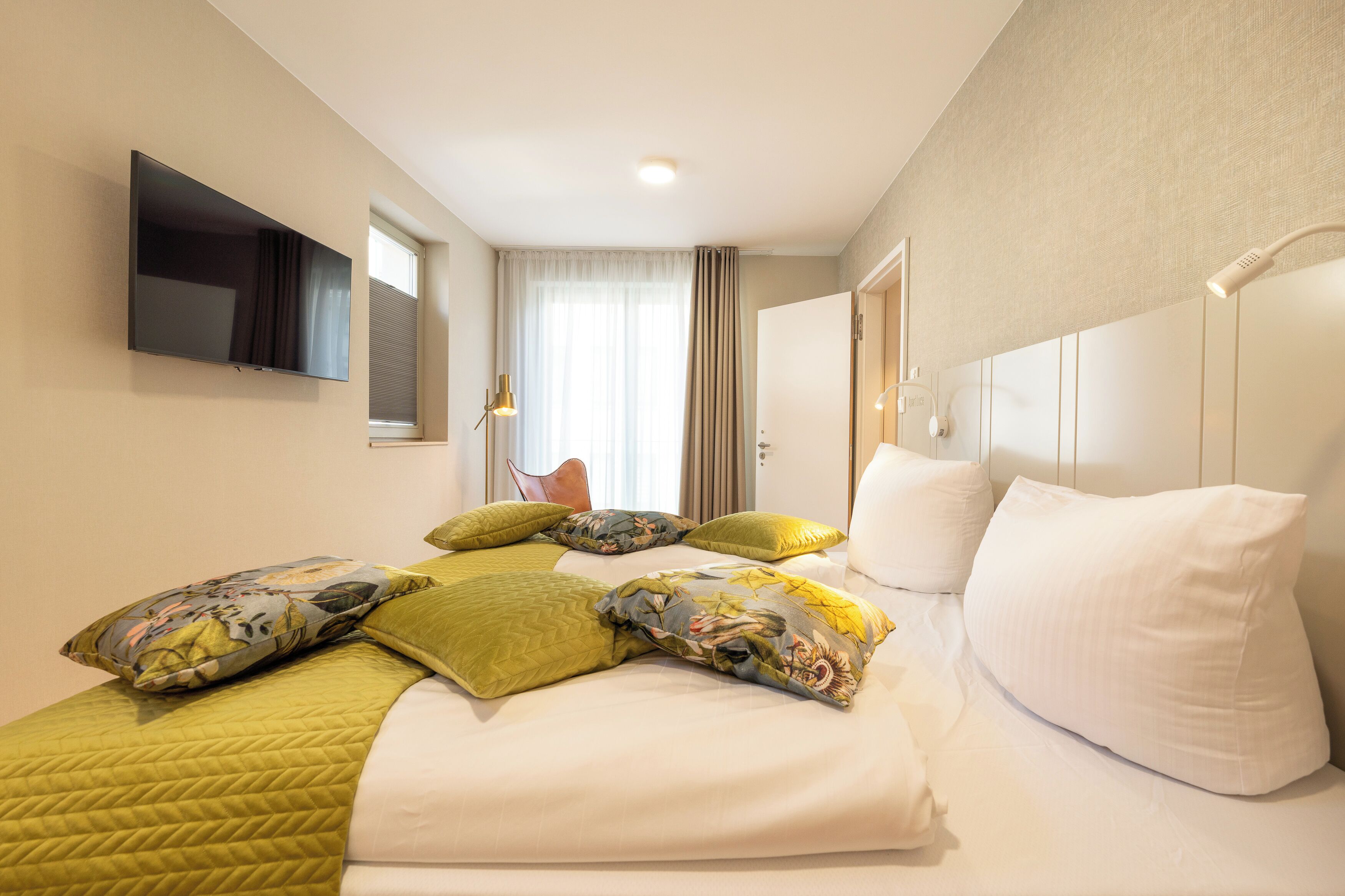 A hotel room with a bed, pillows, a television, and a window with curtains.