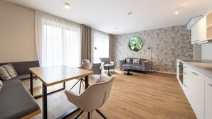 Una sala de estar moderna con sofá, mesa de comedor, sillas, una zona de cocina y una pared decorativa.