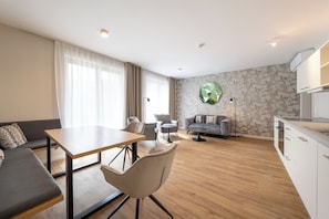 Una sala de estar moderna con sofá, mesa de comedor, sillas, una zona de cocina y una pared decorativa.