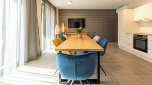 A modern dining area with a wooden table, blue chairs, and a flat-screen TV mounted on the wall.