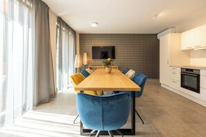 A modern dining area with a wooden table, blue chairs, and a flat-screen TV mounted on the wall.
