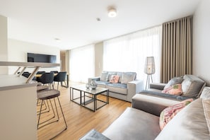 A modern living room with a sofa, coffee table, and dining area. - Design Apartments - Luise (Potsdam)