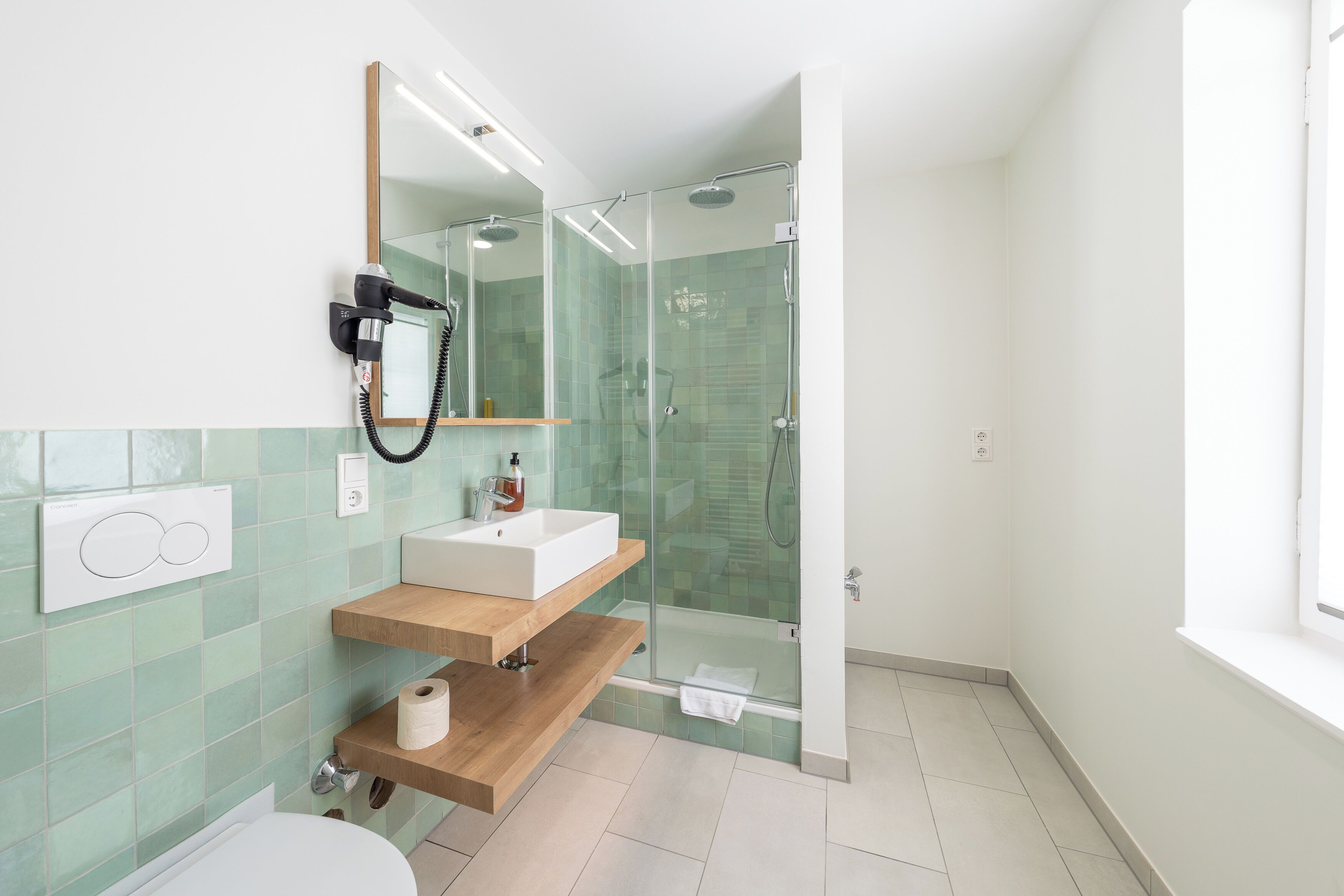 Un baño moderno con ducha envuelta en vidrio, tocador de madera, lavamanos blanco y espejo.