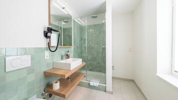 Un baño moderno con ducha envuelta en vidrio, tocador de madera, lavamanos blanco y espejo.