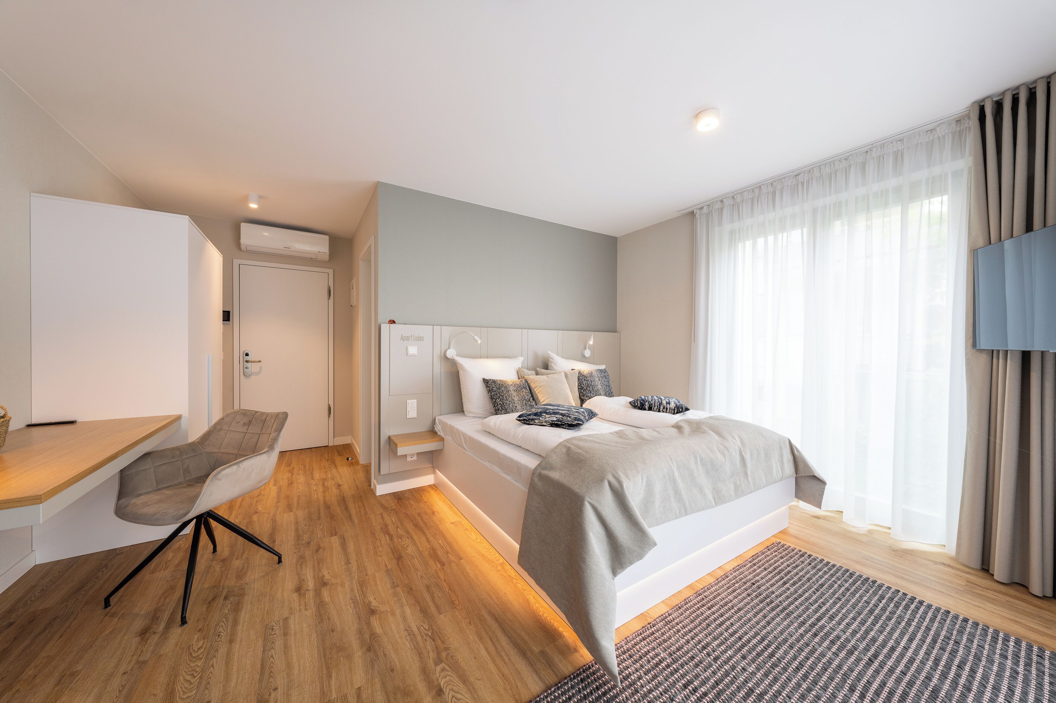Ein modernes Schlafzimmer mit Bett, Nachttisch, Stuhl und Fernseher.
