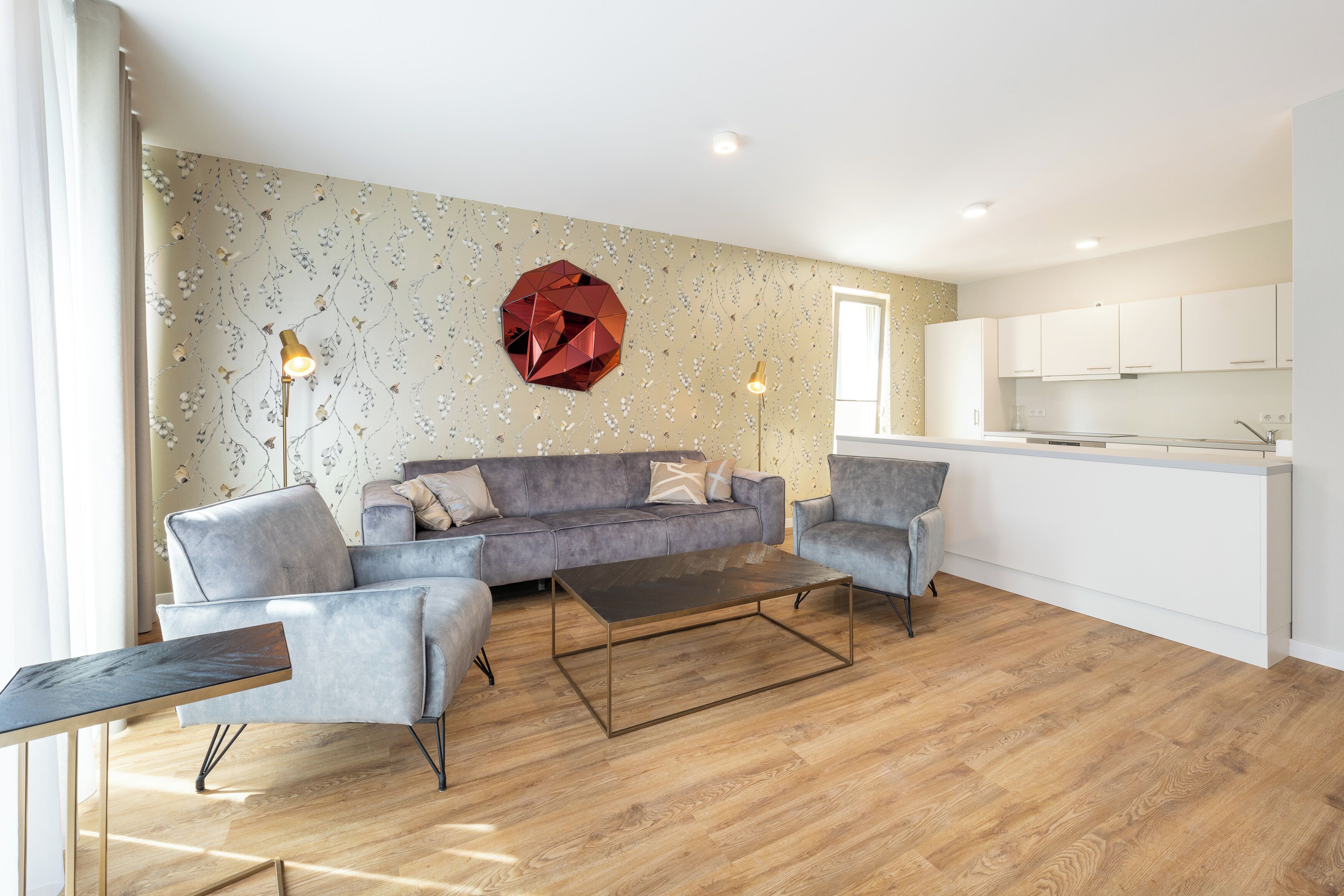 A modern living room with a grey sofa, a coffee table, and a kitchen area with white cabinets.