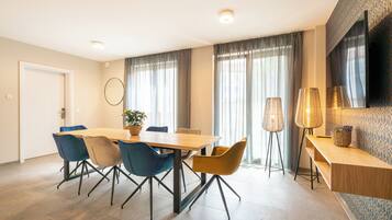 Ein moderner Essbereich mit Holztisch, blau-gelben Stühlen, einer Topfpflanze und einer Stehlampe.