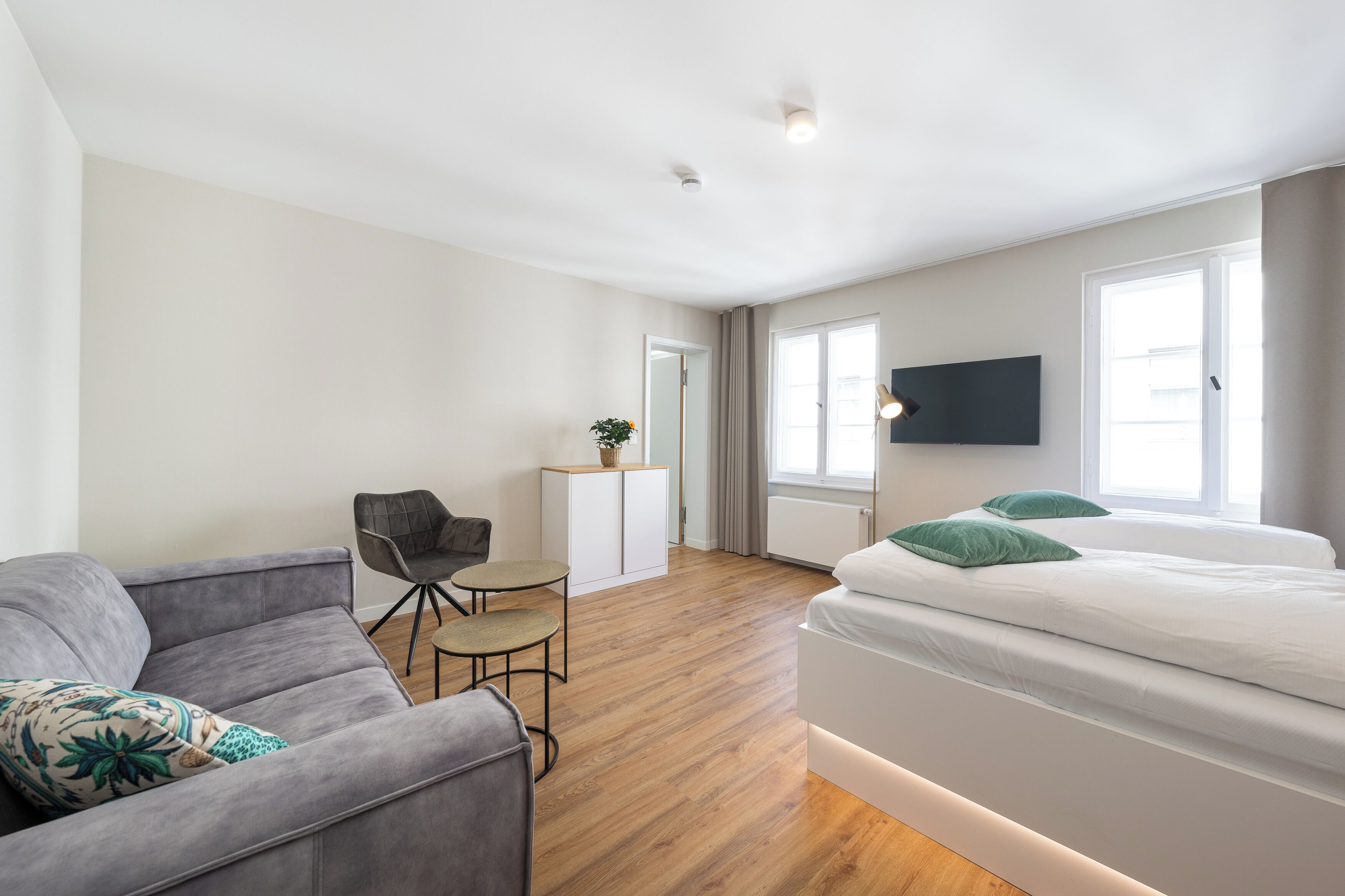 A modern hotel room with a bed, a sofa, a desk, and a TV.
